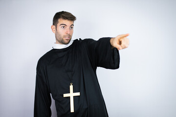 Young hispanic man wearing priest uniform standing over white background pointing with finger...