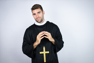 Young hispanic man wearing priest uniform standing over white background with Hands together and...