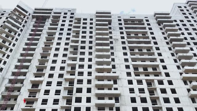 Construction of the high floor house, construction cranes, the bottom view up, slow movement of a video camera, concrete blocks without windows and facade finishing, cloudy weather, a huge real estate