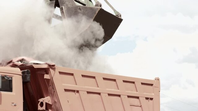 Grapple crane unloading cement clinker from ship to truck in port. Grab is discharging bulk cargo from a hold of cargo ship, causing dust in atmosphere. Loading in Harbor outdoors. Logistics