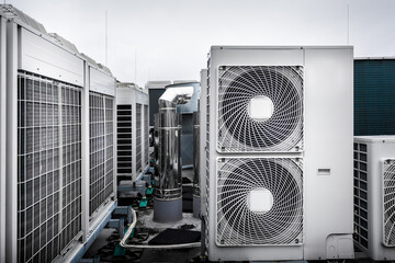 Fototapeta Square air-conditioning units on the roof with round fan grills. In the background gradually receding other units and parts of ventilation system which are out of focus. Sky is uniformly gray. obraz