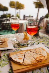 Italian traditional street food and aperitif. Aperol spritz with Piadina or Piada which is a thin Italian flatbread with cheese, ham, rocket, arugula, tomatoes in the northern Italy, Lombardy, Milan.