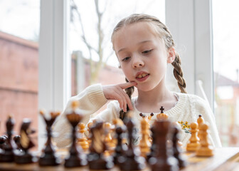 Beautiful cute genius child young girl playing chess strategy with wooden pieces on chessboard kid...