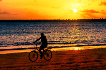 Fototapeta premium Silhueta de homem andando de bicicleta na praia de Serrambi durante o pôr-do-sol.