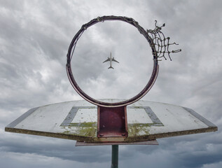 A plane flying over the basketball hoop. - obrazy, fototapety, plakaty