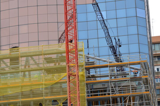 Grua sobre el edificio de construccion, fondo con edificio de oficinas, reflejada en las ventanas