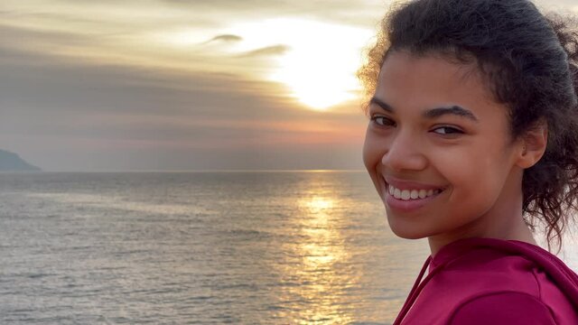 Wonderful morning. Close up of young woman looking aside and then smiling at camera, admiring the sea view at sunrise. Slow motion. Copy space on the left side