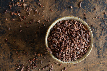 organic cacao nibs from Peru in clay bowl on abstract wooden background