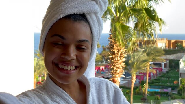 Super resort. Joyful young woman in bathrobe taking selfie while standing on the hotel balcony with sea view. Lockdown is over. Time to travel. Vacation, technology concept