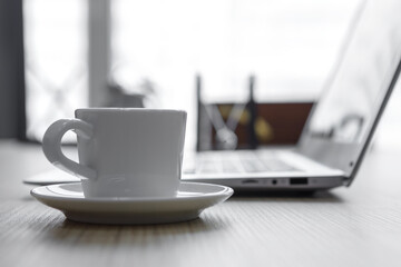 A cup of coffee on the desk in the office against the background of a laptop.