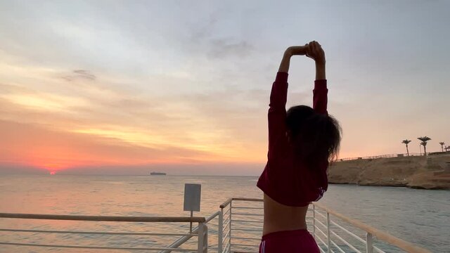 The beauty of nature. Sportive young woman doing morning exercises on the pier at sunrise. Slow motion. Healthy lifestyle, nature concept