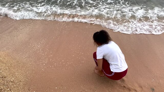 Spend time near the sea. Young mixed race woman collecting seashells on the beach. Vacation, leisure concept. Slow motion
