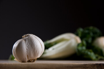 Garlic on wood cutting board with bok choy in the background