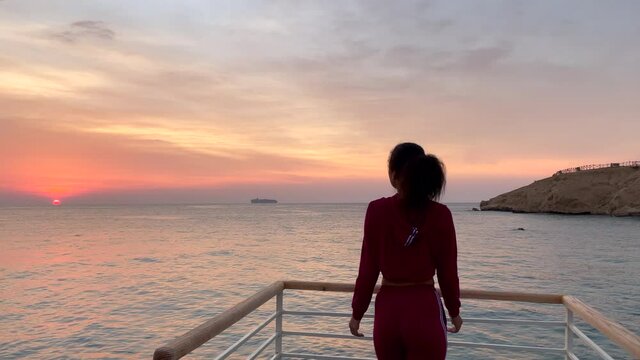 Morning sky. Rear view of young woman walking to the edge of the pier and admiring the dawn. Slow motion. Lifestyle, nature concept