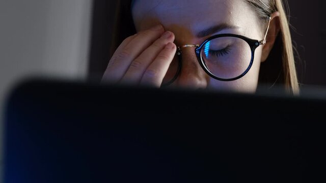 Young sad woman taking off glasses feels eye strain tension tired of computer sitting in bed with laptop, unhappy tired girl has bad sight vision problem massaging dry eyes after long laptop use