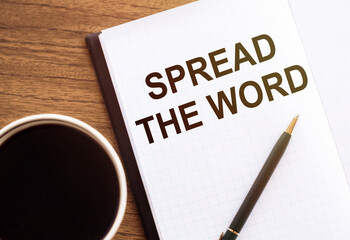 SPREAD THE WORD - text on notepad on wooden desk.