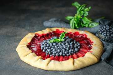 Homemade galette with blueberries and plums with milk on a dark background.