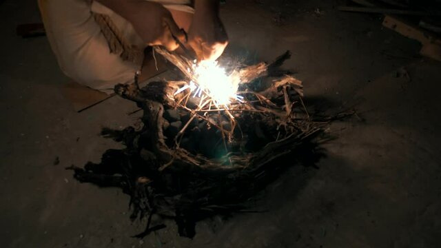 Ancient man tries to light a large bonfire at night in a cave