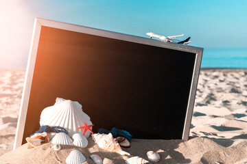 Summer sale. Globe, seashell, airplane and starfish near black desk on sea beach in sunny day. Copy space of summer vacation and business travel concept.
