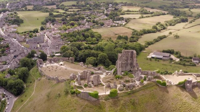 Aerial tracking shot behind Corfe Castle, Dorset, UK with the village and civil parish in the background