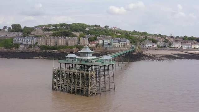 Aerial tracking past Victorian Clevedon Pier over the Severn Estuary on a sunny day with Clevedon town in the background, Somerset, United Kingdom