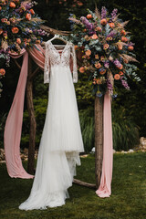 Wedding dress hanging on wedding gate with rich colorful luxury flower and pink decoration in outdoor