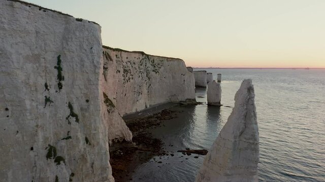 Aerial reveal of sunrise over sea through chalk cliff rock stacks at Old Harry rocks in Dorset, England's Jurassic coast