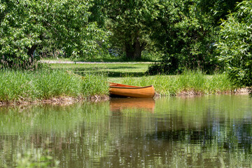 Cedar wood canoe on land at the edge of a pond - tall gasses and trees make up a rich green background