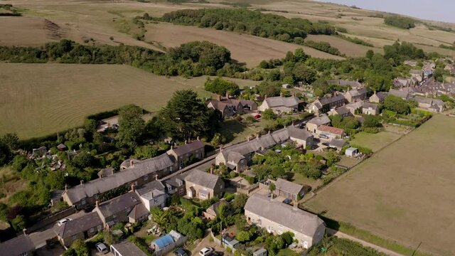 Aerial tracking through traditional idyllic English village of Abbotsbury in Dorset on a summer's day - past rows of quaint houses in a picturesque countryside setting