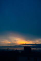view on atmospheric sunset in blue, yellow and orange tones over sea and dark silhouettes of residential buildings. vertical travel content. selective focus