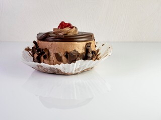 Chocolate mini cake with chocolate frosting, curled chocolate and a berry on top, sitting on a white counter with the reflection showing, a delicious indulgence of a sweet dessert waiting to be eaten.