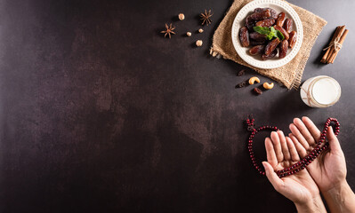 Ramadan Kareem background concept, Hands holding rosary bead with dates fruit and milk on dark stone background.