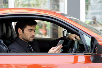Young businessman in a black suit look at mobile phone while holding the car wheel.