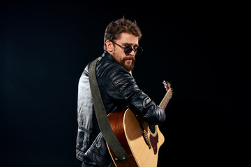 Fototapeta premium man with a guitar in his hands black leather jacket sunglasses music emotions black background