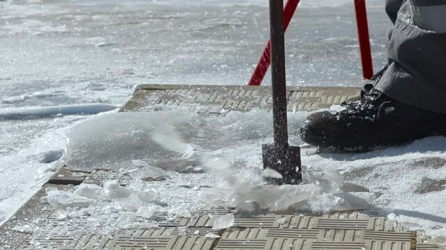 The worker hits the ice with a crowbar and splashes and snow crystals fly. Close-up from the bottom point of the image. Cleaning the sidewalk surface from ice.