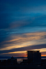 Fototapeta na wymiar view on atmospheric sunset in blue, yellow and orange tones over sea and dark silhouettes of residential buildings. vertical travel content. selective focus