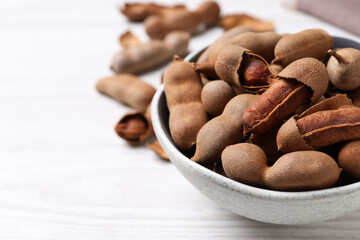Delicious ripe tamarinds in ceramic bowl on white wooden table, closeup. Space for text