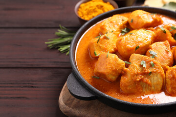 Fototapeta premium Delicious chicken curry in pan on wooden table, closeup. Space for text