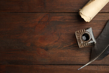 Feather pen, inkwell and parchment scroll on wooden table, flat lay. Space for text
