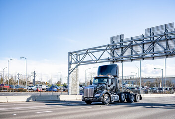 Black shiny clean day cab big rig semi truck tractor running on the wide highway interstate road to warehouse for pick up a semi trailer with next delivery load