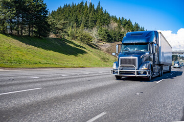 Fototapeta na wymiar Blue big rig semi truck with pipe grille guard transporting commercial cargo in dry van semi trailer running on the flat straight highway road in front of another track