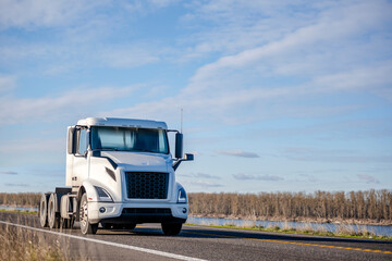 Compact day cab white big rig semi truck tractor without semi trailer running on the road along the...