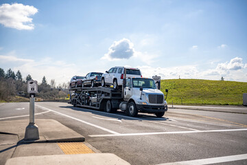 Compact white big rig car hauler semi truck transporting cars on the two level module semi trailer...