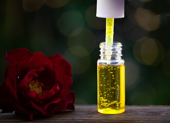 Bubbles in the brightly lit yellow oil in an oil dropper bottle contrast with the nature blurred...