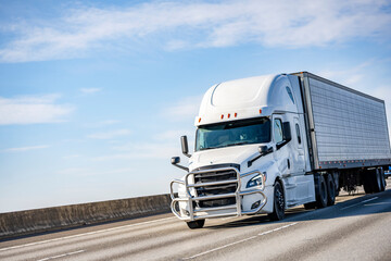 Powerful white big rig long haul industrial semi truck transporting goods in refrigerator semi...