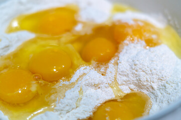 Fresh raw yellow chicken eggs with flour close-up. Mix the broken raw eggs and wheat flour to make the pancakes.The concept of healthy eating. Food background. Preparation of the dough.Organic product