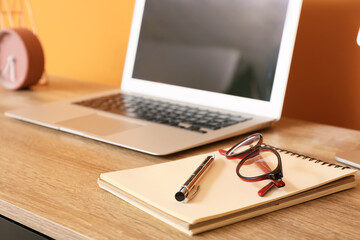 Laptop, notebook and eyeglasses on table in office