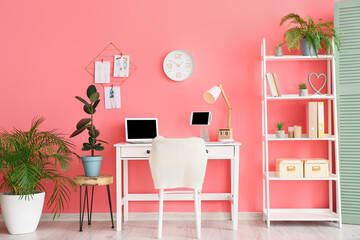 Stylish workplace with laptop near color wall in office