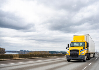 Fototapeta na wymiar Yellow day cab big rig semi truck tractor for local deliveries transporting cargo in dry van semi trailer running on the wide highway road with stormy clouds sky