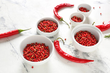 Bowls with red peppercorns and chili pepper on light background